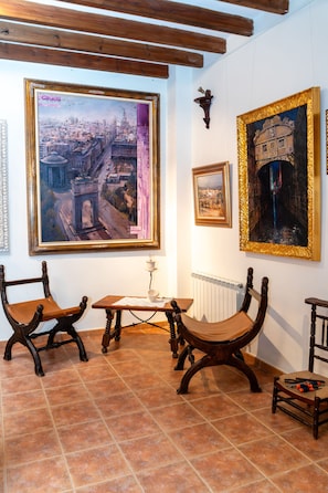 A room with a large cityscape painting, a smaller framed painting, and two antique chairs.