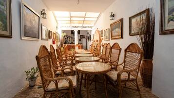 Un comedor con sillas de mimbre y mesas redondas, obras de arte en las paredes y un tragaluz.