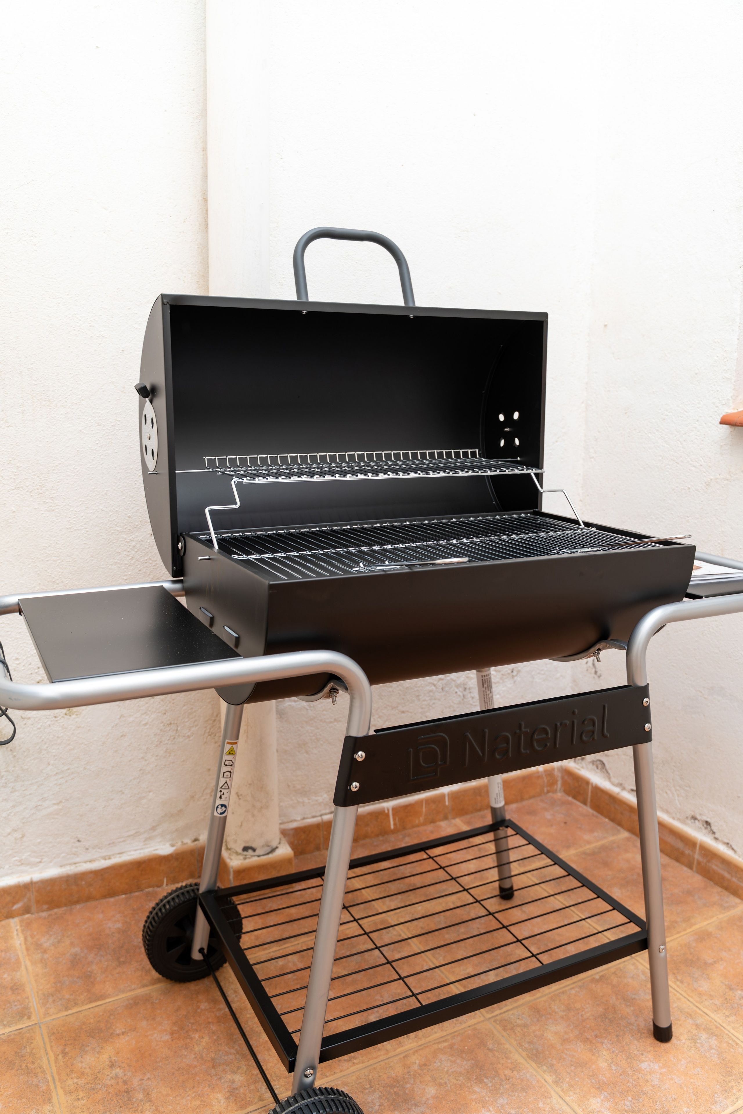 Una parrilla portátil para barbacoa con carro metálico, ruedas y asa.