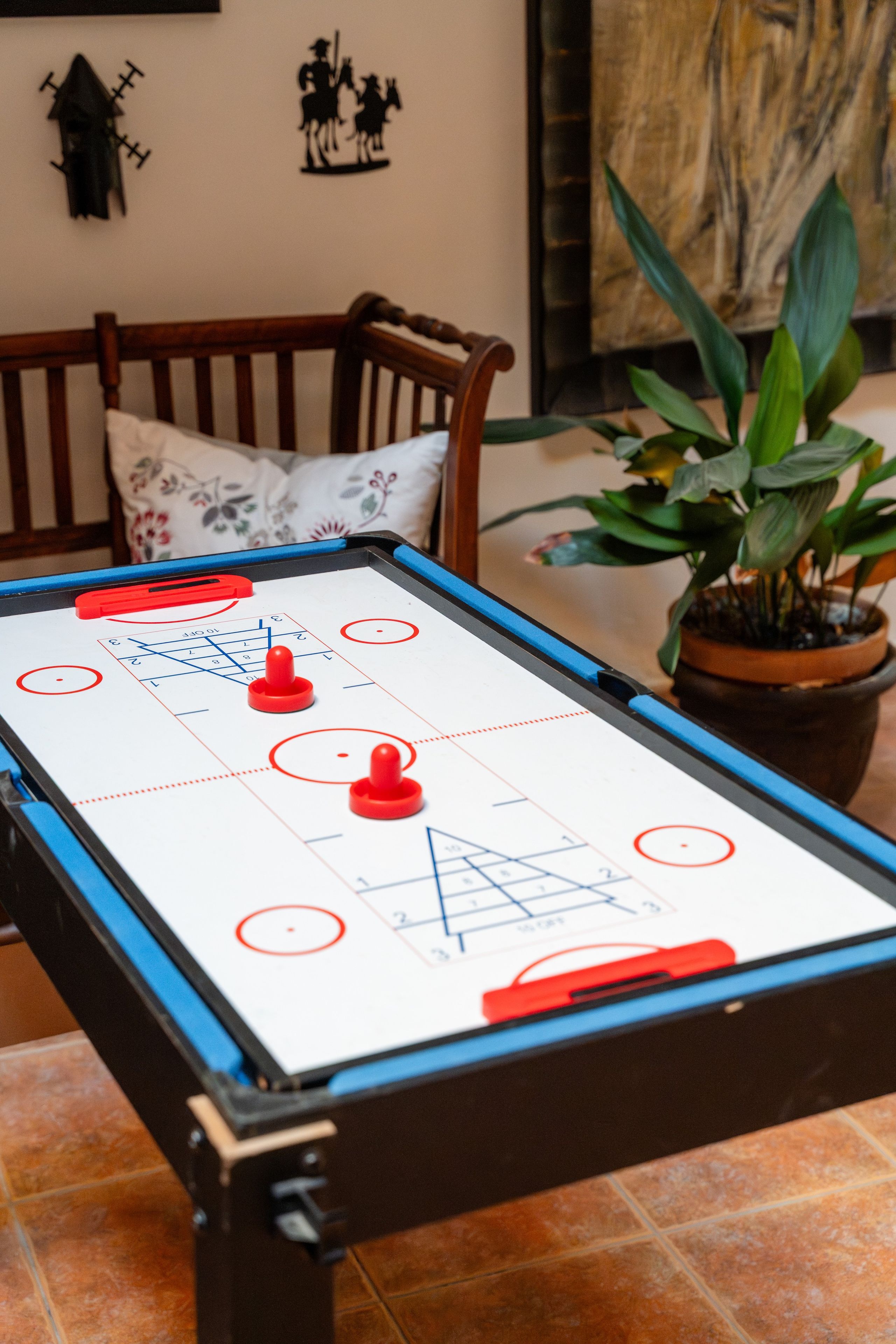 Une table de billard avec une partie en cours, une chaise en bois, une plante en pot et un mur orné d’un élément décoratif.