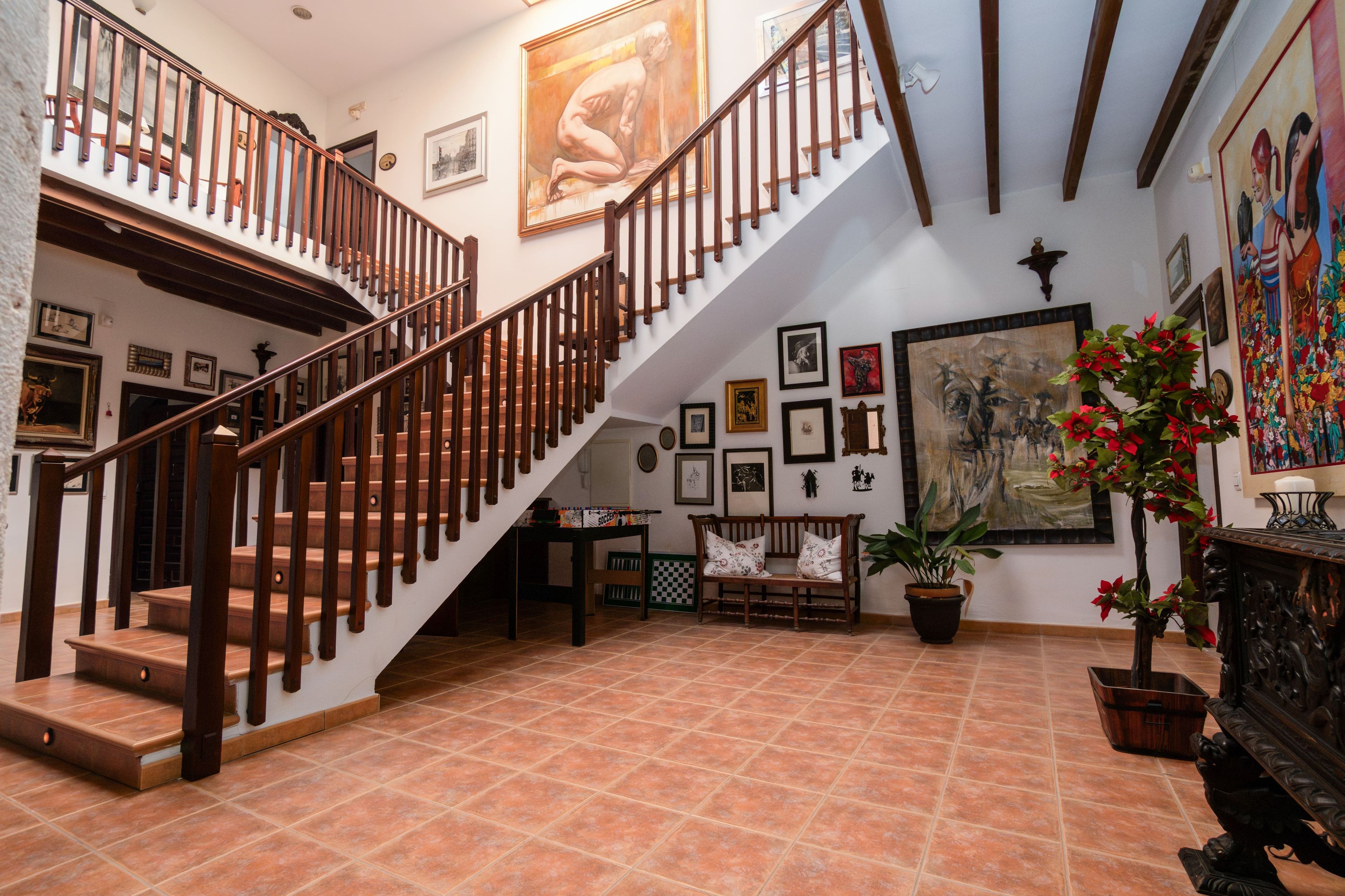 A staircase with wooden railings leading to an upper level, surrounded by framed artwork and a potted plant.