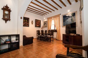 A living room with a dining area, a television, and a clock on the wall.