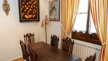 Un comedor con una mesa y sillas de madera, un cuadro enmarcado con naranjas y una ventana con cortinas a rayas.