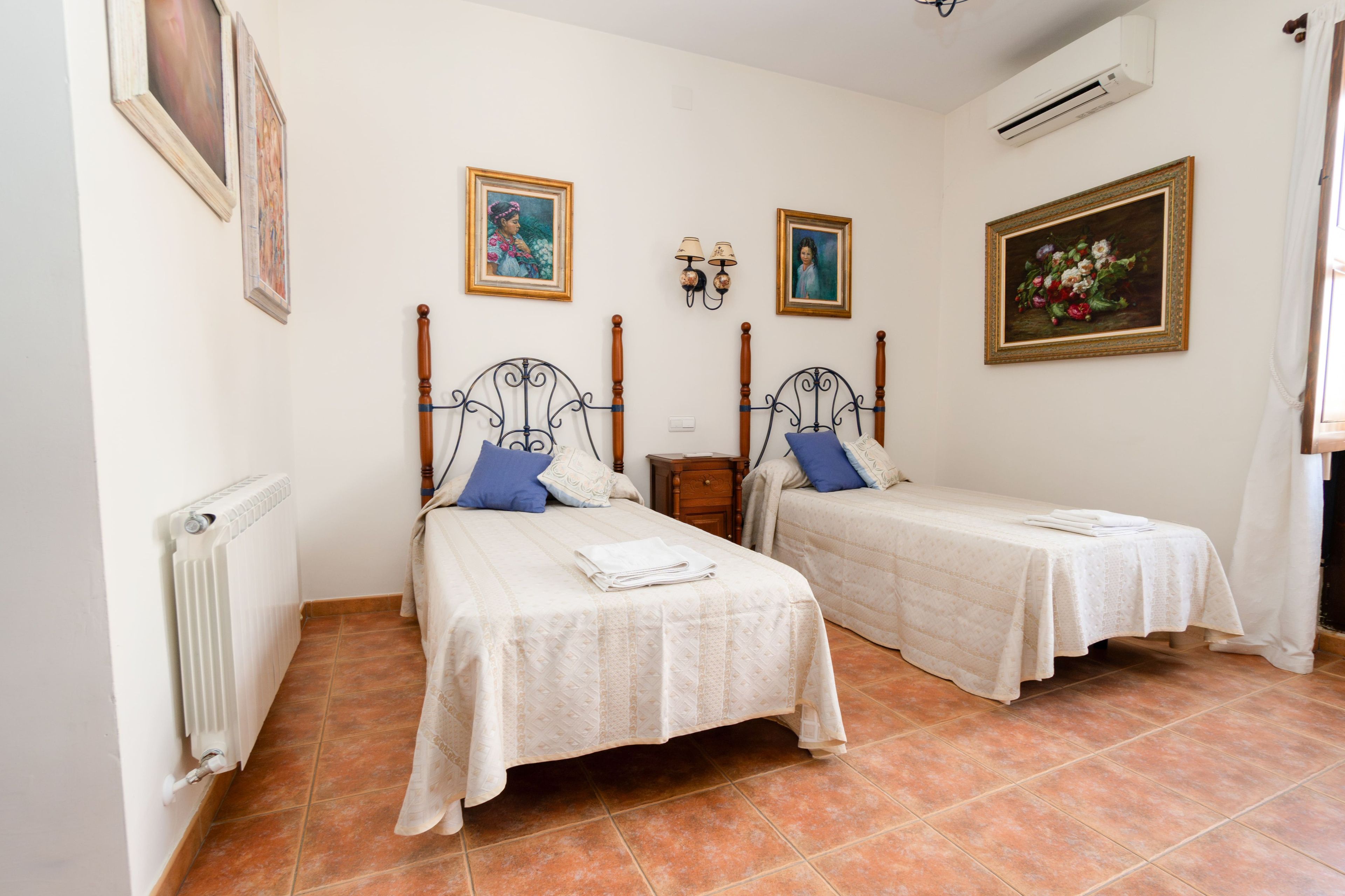 Una habitación con dos camas individuales, un radiador, aire acondicionado de pared y dos lámparas de pared.