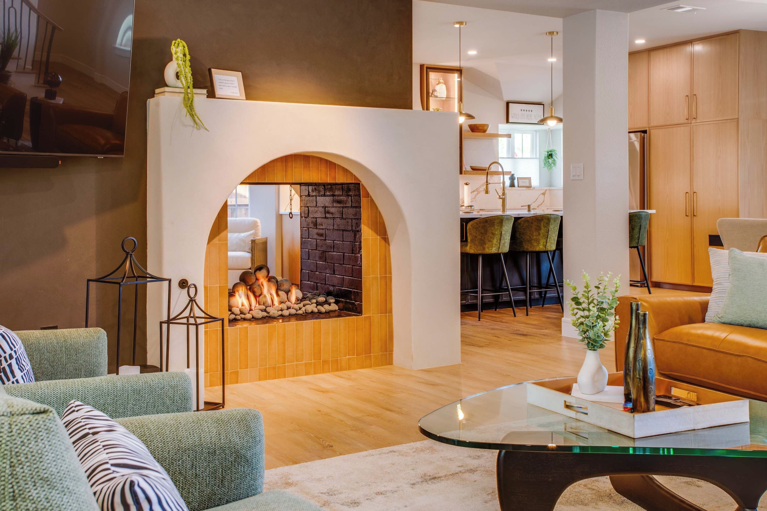 A modern living room with a fireplace, seating area, and kitchen in the background.