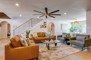 A spacious living room with a staircase, leather sofas, a glass coffee table, and a ceiling fan. - Richardson Retreat - Pool, Hot Tub & Fire Pit (Richardson)