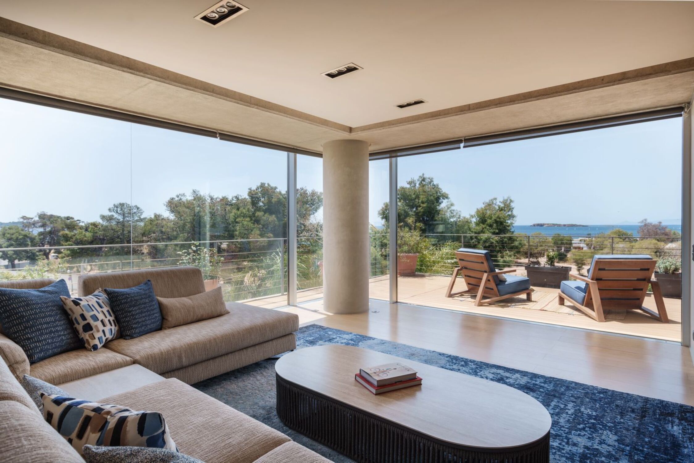 A modern living room with a large sofa, a coffee table, and a view of the outdoors through floor-to-ceiling windows.