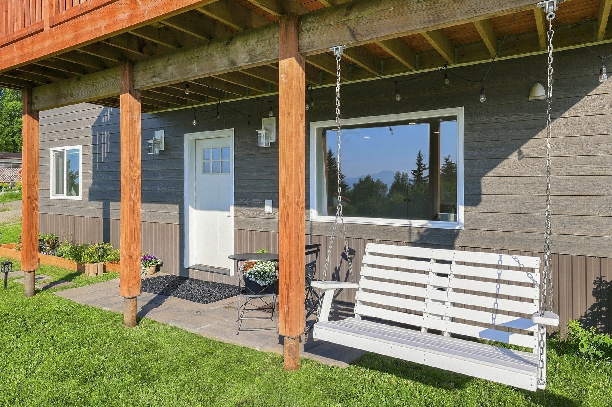 Une cabane en bois avec une véranda, une porte blanche, une fenêtre, un banc et une table avec des chaises.
