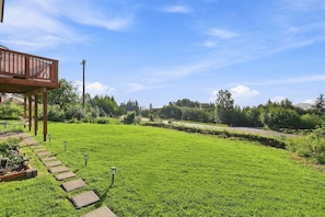 A well-maintained lawn with a wooden deck and stone pathway leading to a house. - Modern 2BR suite with glacier views (Homer)