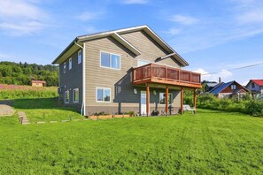 A two-story house with a balcony, a grassy yard, and neighboring houses. - Modern 2BR suite with glacier views (Homer)