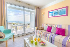 A room with a balcony, a striped sofa, a table with a teapot and fruit, and a view of the sea. - Oceanfront Suite for Five (Les Sables-d'Olonne)