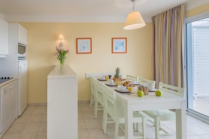 Una cocina moderna con electrodomésticos blancos, un comedor con mesa y sillas blancas, y un amplio ventanal con cortinas.