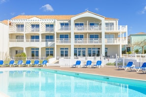 Un hotel de varios pisos con piscina, balcones y tumbonas.