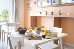 Desayuno con croissants, zumo de naranja y un periódico sobre una mesa con sillas blancas.