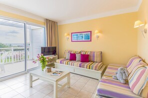 A room with a sofa, a television, a table with a magazine, and a vase of flowers. - Oceanfront Suite for Five (Les Sables-d'Olonne)