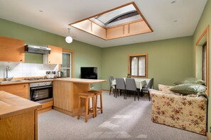 A compact kitchen with a central island, a dining area with a table and chairs, and a cozy seating area with floral cushions. - Riverbank Lodge Annexe (Datchet)