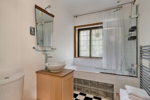 Ein Badezimmer mit Toilette, Waschbecken, Spiegel, Dusche und einem Fenster mit Jalousien.