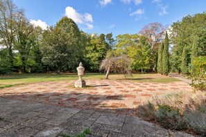 A garden with a paved area, a stone fountain, and various trees. - Riverbank Lodge Annexe (Datchet)