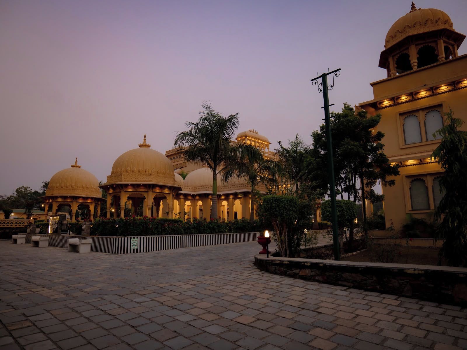 A courtyard with a large building featuring domed structures and a smaller building with a dome.