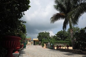 A paved pathway leading to a building with a traditional architectural style, surrounded by lush greenery and palm trees. - Tathastu Heritage Resort (Udaipur)