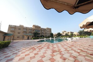 A pool area with a checkered floor, a building with multiple windows, and a clear sky. - Tathastu Heritage Resort (Udaipur)