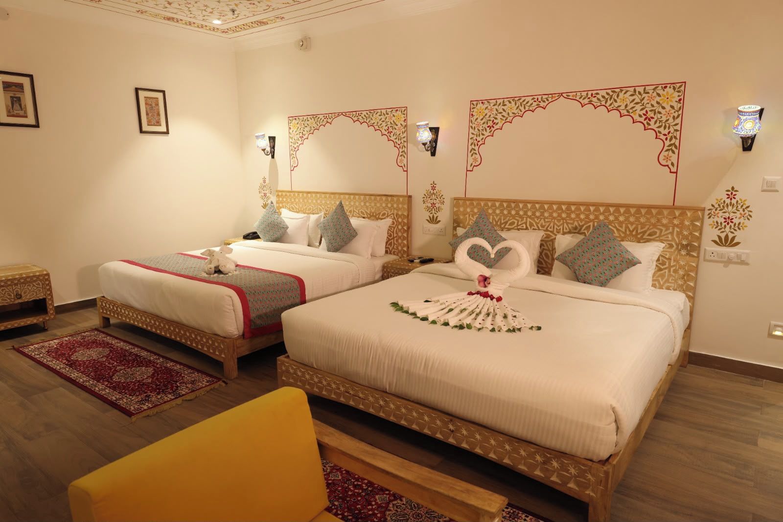 A hotel room with two beds, a red and a white bedspread, a wooden headboard, a small yellow chair, and a red patterned rug.