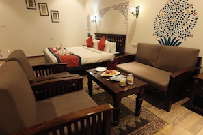 A hotel room with a bed, two sofas, a coffee table with breakfast items, and decorative wall art. - Tathastu Heritage Resort (Udaipur)