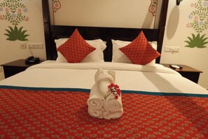 Habitación de hotel con una cama bien hecha, colcha estampada de color rojo y almohadas decorativas.