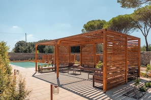 A wooden pergola structure with seating and a pool in the background.