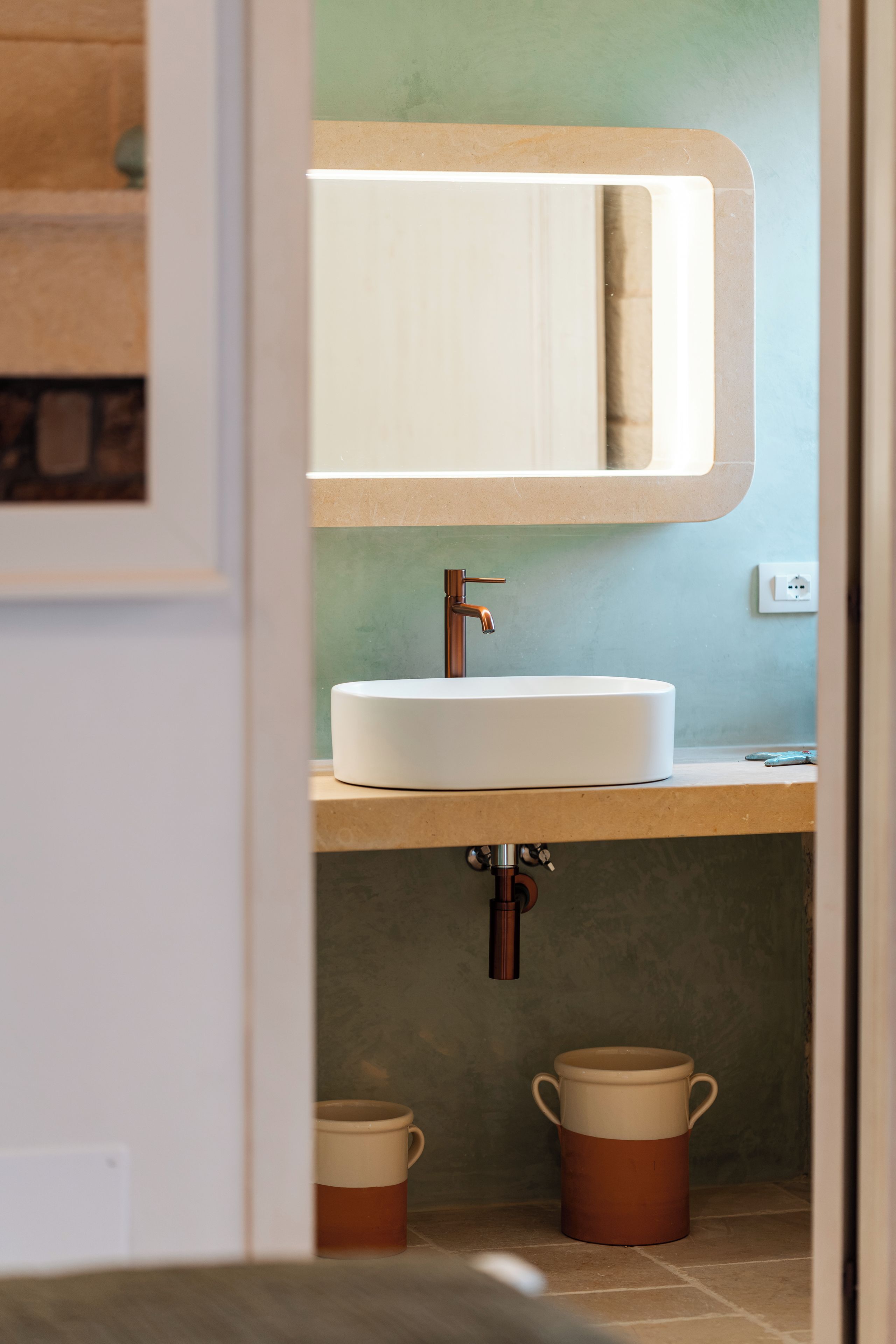 A bathroom with a white sink, a mirror, and two brown mugs on the floor.