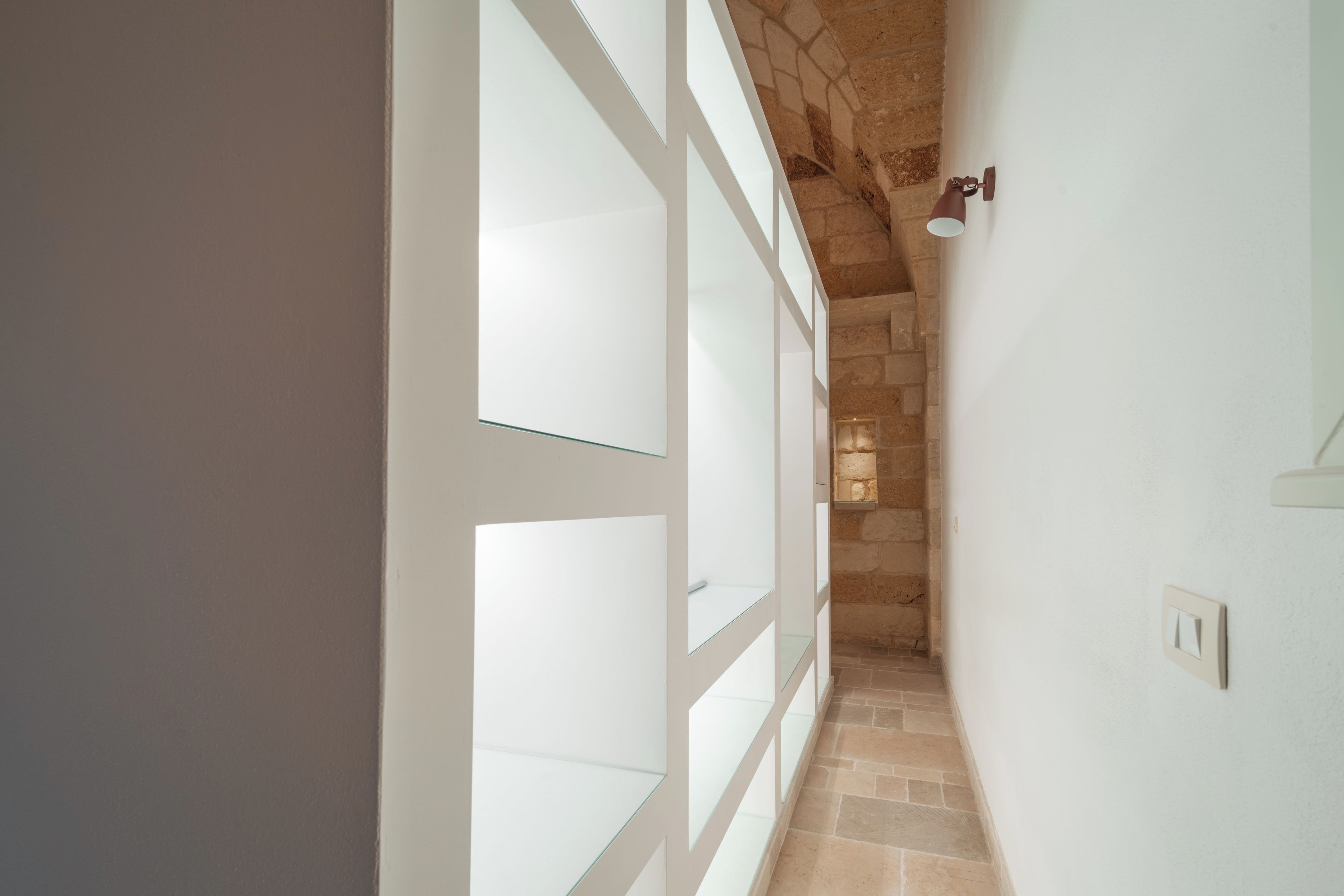 A narrow hallway with a stone wall and a glass door on the left.