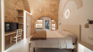 A bedroom with a stone wall, a bed with white bedding, a television, and a desk with a chair.
