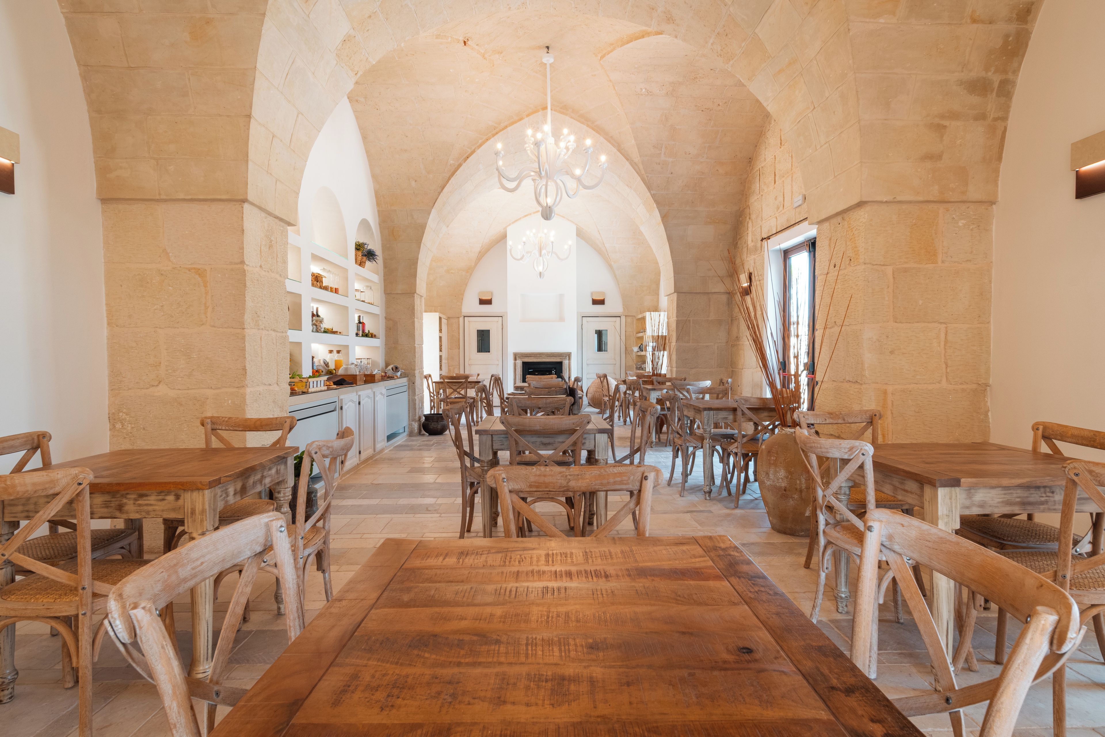 Un hallo espacioso con altos arcos de piedra, mesas y sillas de madera y una lámpara central.