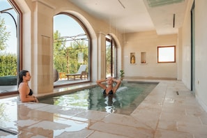 Piscina interior ampla com água cristalina, rodeada por grandes janelas e vista para o verde lá fora.