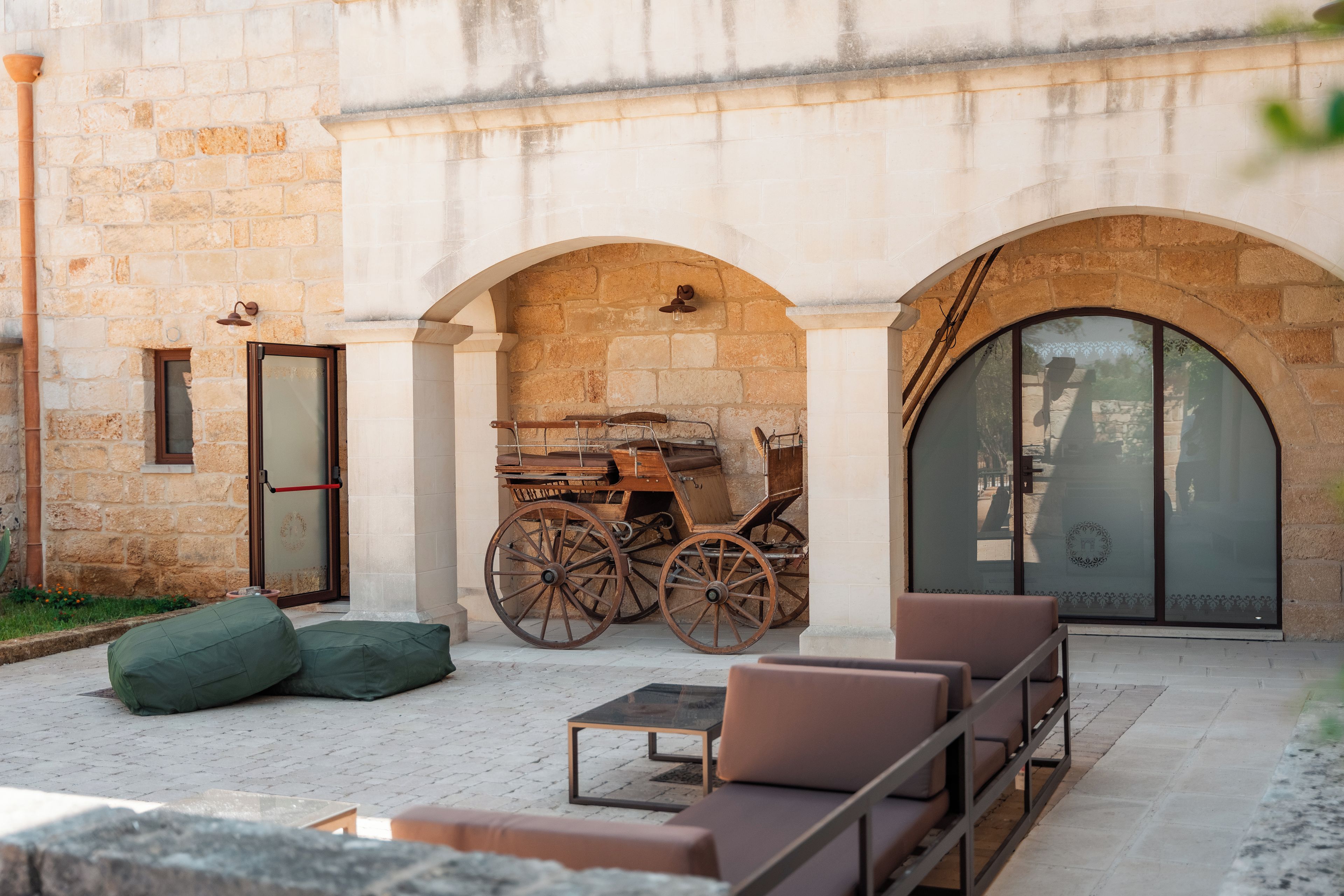 An outdoor seating area with stone walls, a wooden cart, and a glass door.