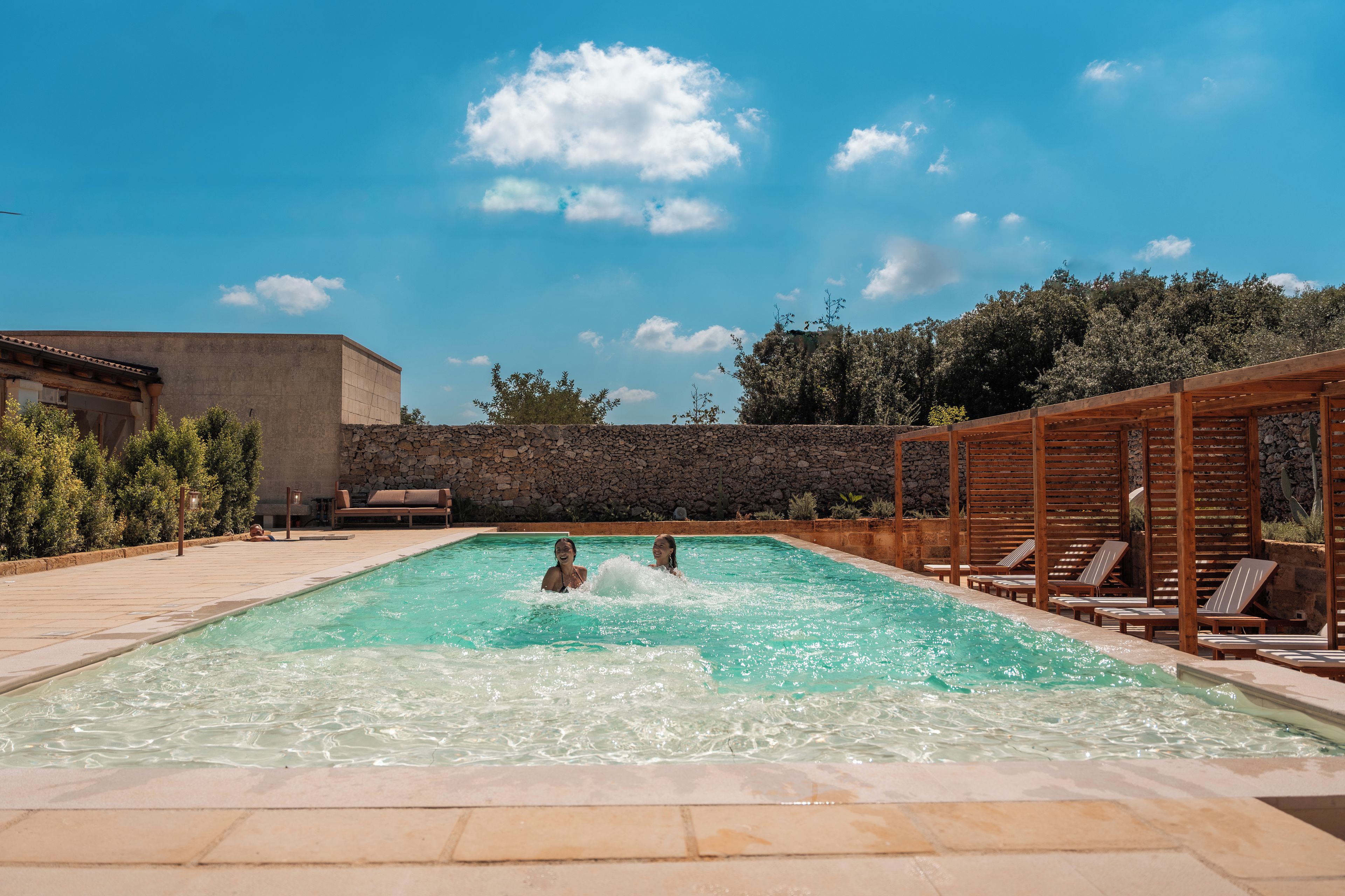 A swimming pool with lounge chairs and a stone wall.
