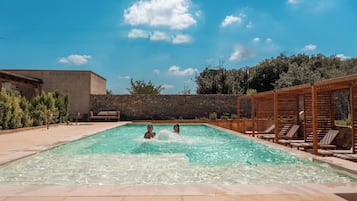 A swimming pool with lounge chairs and a stone wall.