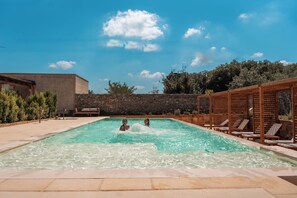 A swimming pool with lounge chairs and a stone wall.