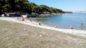 Une plage où des gens se prélassent au soleil et se baignent, entourée d’arbres et sous un ciel dégagé.