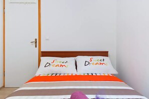 Un lit avec deux oreillers, chacun orné de l’inscription « Doux rêves », et une couvre-lit à rayures.