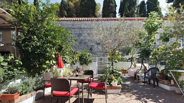 Une terrasse avec une table et des chaises, entourée de plantes en pot et d’un mur de pierres.