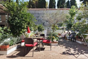 Une terrasse avec une table et des chaises, entourée de plantes en pot et d’un mur de pierres.