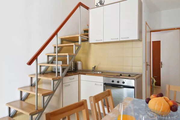 Une cuisine avec un escalier en bois, des armoires blanches, un évier en acier inoxydable et un coin repas avec des chaises et une table.