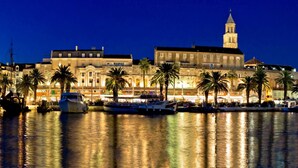 Un hôtel situé au bord de l’eau, avec un grand bâtiment caractérisé par une tour imposante, de nombreux balcons et son reflet dans l’eau.