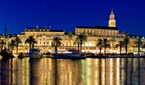 A waterfront hotel with a large building featuring a prominent tower, multiple balconies, and a reflection in the water. - Apartment with large garden in the heart of Split (Split)