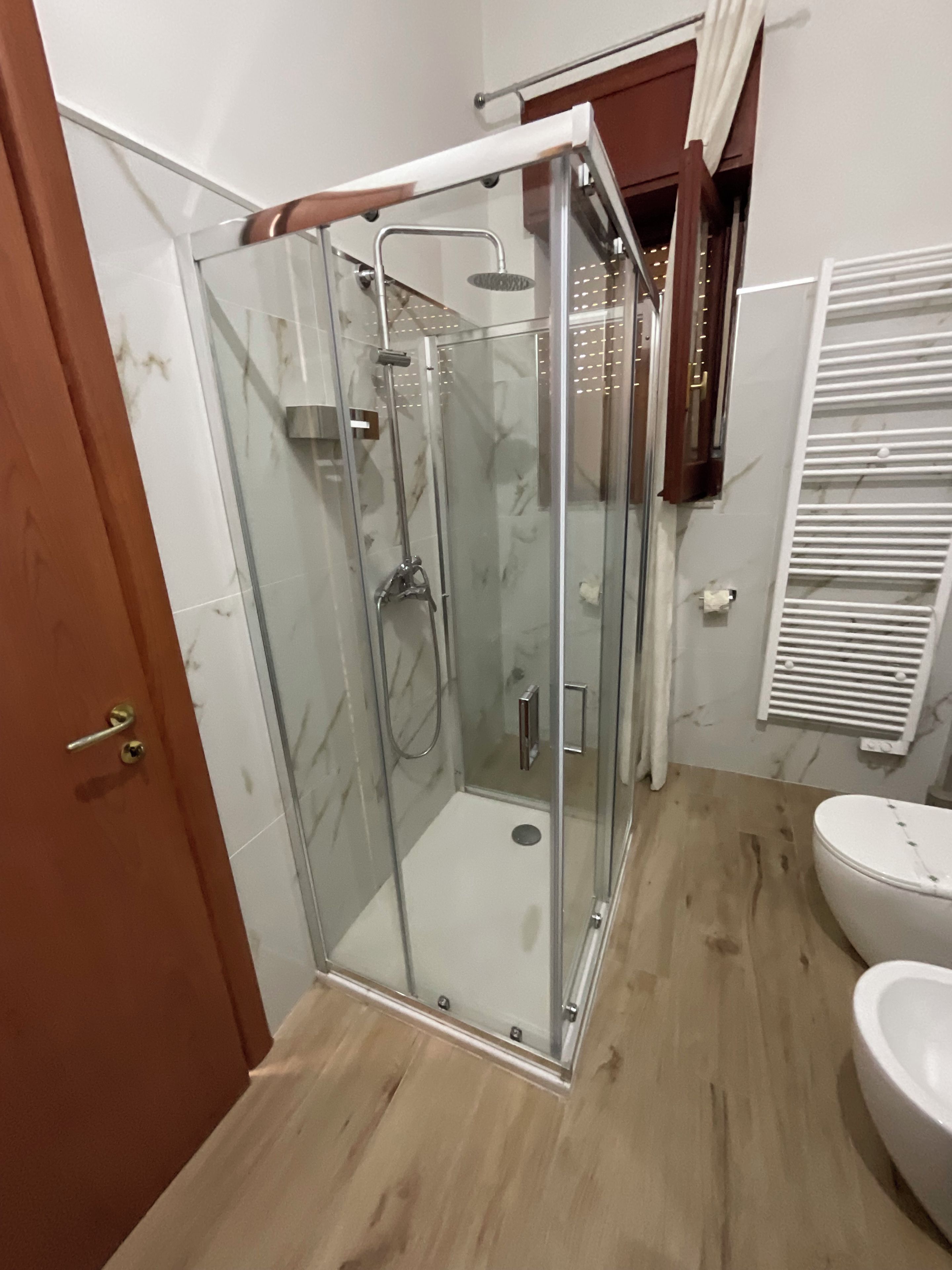 Een douchecabine met glazen wanden, een handdouche en een muurbevestigde kraan.