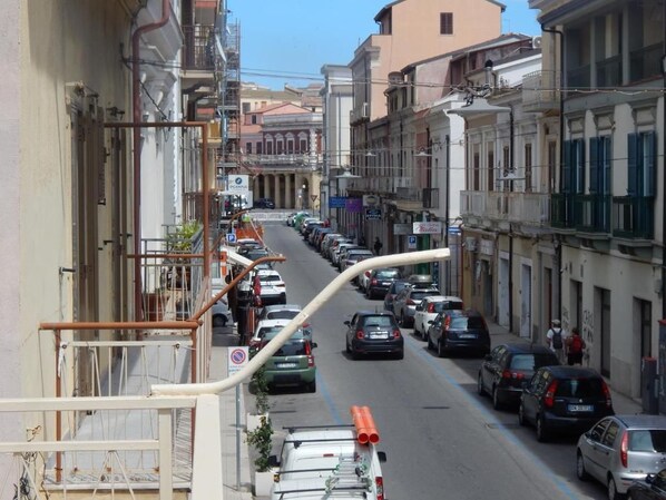 A narrow street lined with parked cars and buildings with balconies.