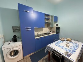 Una cocina compacta con armarios azules, un microondas integrado y una estufa a gas.