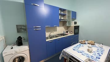 A compact kitchen with blue cabinets, a washing machine, and a table with a tablecloth.