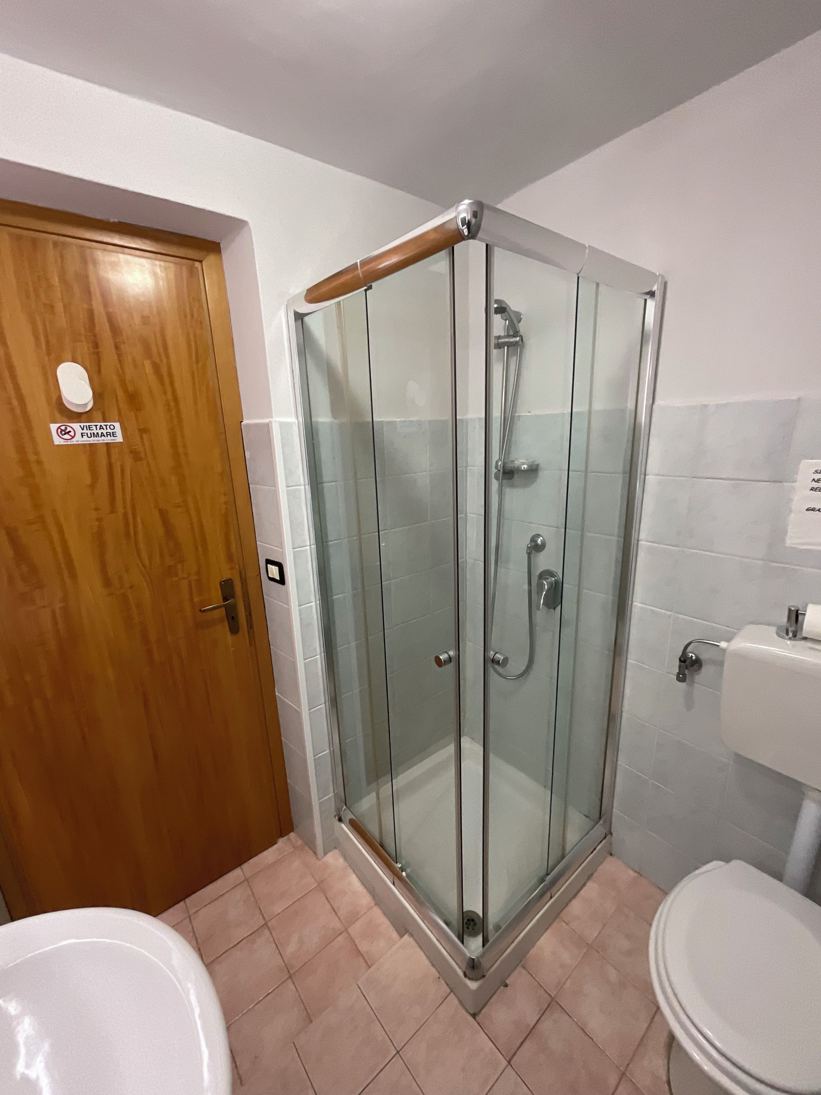 Un bagno con cabina doccia in vetro, una porta in legno con il cartello 'No Smoking', un lavandino bianco e un water.